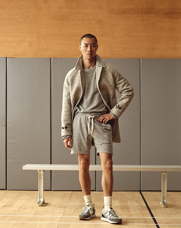 Studio shot of a young Asian man in casual fashion: gray sweater, shorts, overcoat and running shoes, posing against a neutral background.