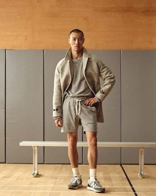 Studio shot of a young Asian man in casual fashion: gray sweater, shorts, overcoat and running shoes, posing against a neutral background.