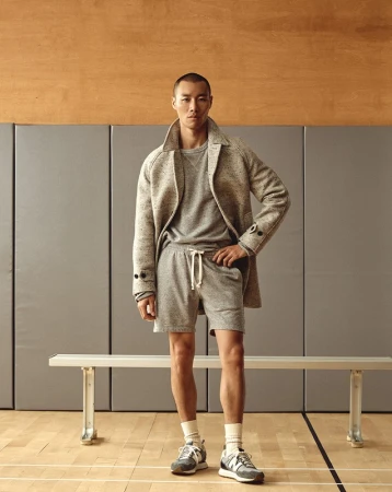 Studio shot of a young Asian man in casual fashion: gray sweater, shorts, overcoat and running shoes, posing against a neutral background.