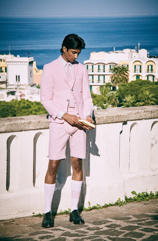 Man in pink suit and shorts poses in front of cityscape with the ocean. He's wearing white socks and dark shoes outdoors.