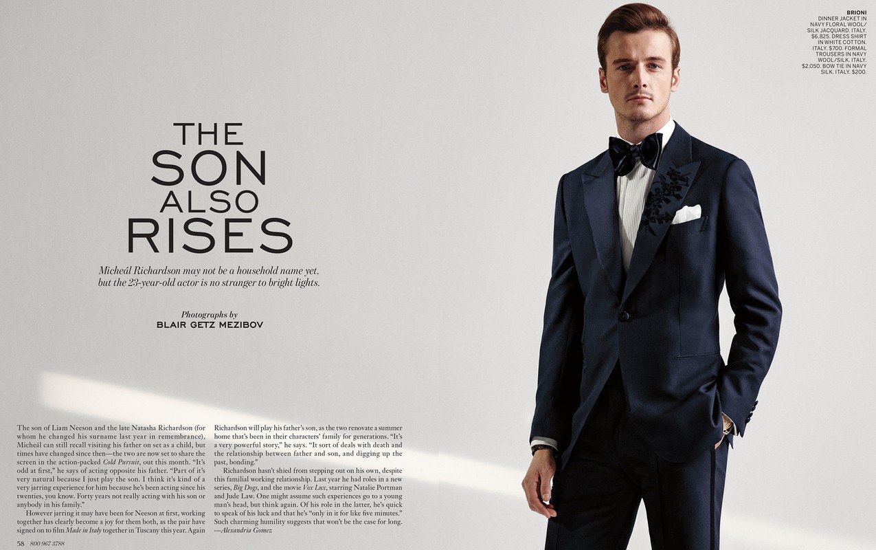 Portrait of a young adult male in a navy blue floral dinner jacket with bow tie and white dress shirt against a plain background.