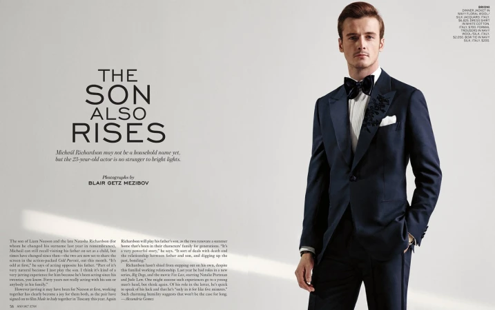 Portrait of a young adult male in a navy blue floral dinner jacket with bow tie and white dress shirt against a plain background.