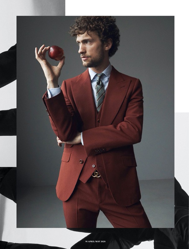 Adult man in a red suit holding a red apple against a grey backdrop. Fashion editorial shot in a photo studio.