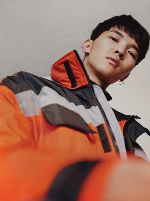 Portrait of a young adult male in a colorful jacket, looking slightly downward towards the camera in a high angle, indoor studio shot.