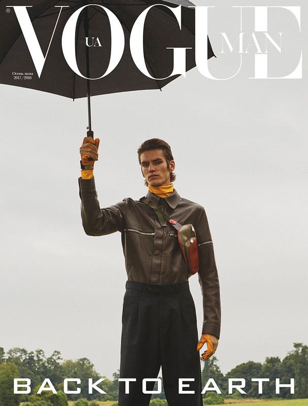 Vogue Man magazine cover featuring a man in a brown jacket and black pants holding an umbrella, set against a field backdrop.