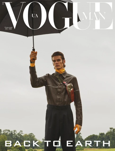 Vogue Man magazine cover featuring a man in a brown jacket and black pants holding an umbrella, set against a field backdrop.