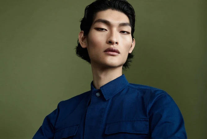 Portrait of an East Asian man wearing a blue shirt against an olive green backdrop