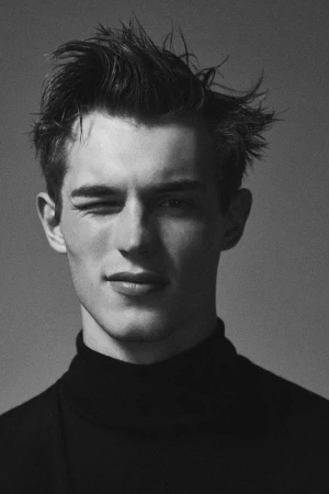 Portrait of a man in a black turtleneck winking with tousled hair against a plain grey backdrop.