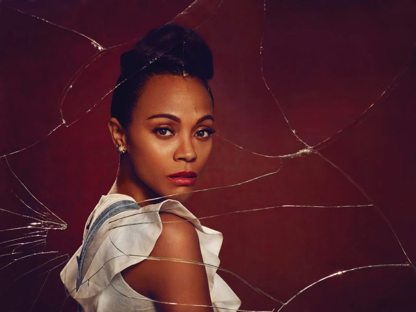 Portrait of actress Zoe Saldana looking over her shoulder with shattered glass effect in foreground and dark red background.