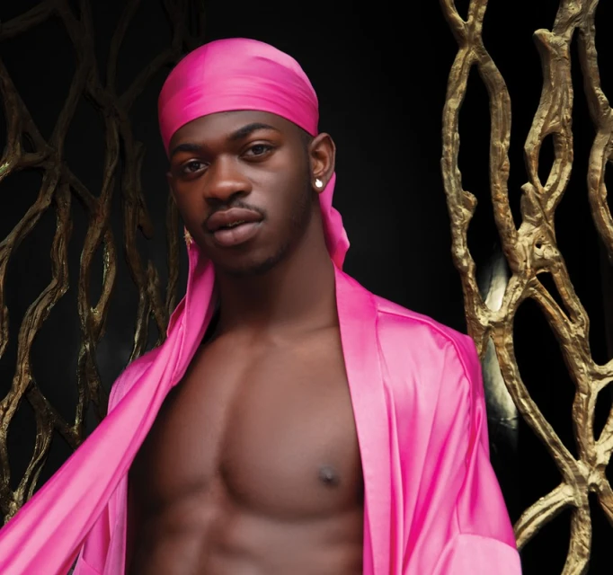 Portrait of an adult male with dark skin wearing a pink headscarf and robe, posing in front of an ornate gold sculpture.