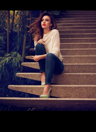 Jessica Alba seated on outdoor concrete steps wearing a white blouse, blue jeans, and light green heels, photographed in Los Angeles.