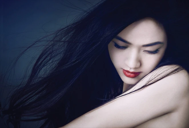 Close-up portrait of a woman with long dark blowing hair and vibrant red lipstick captured by James White.