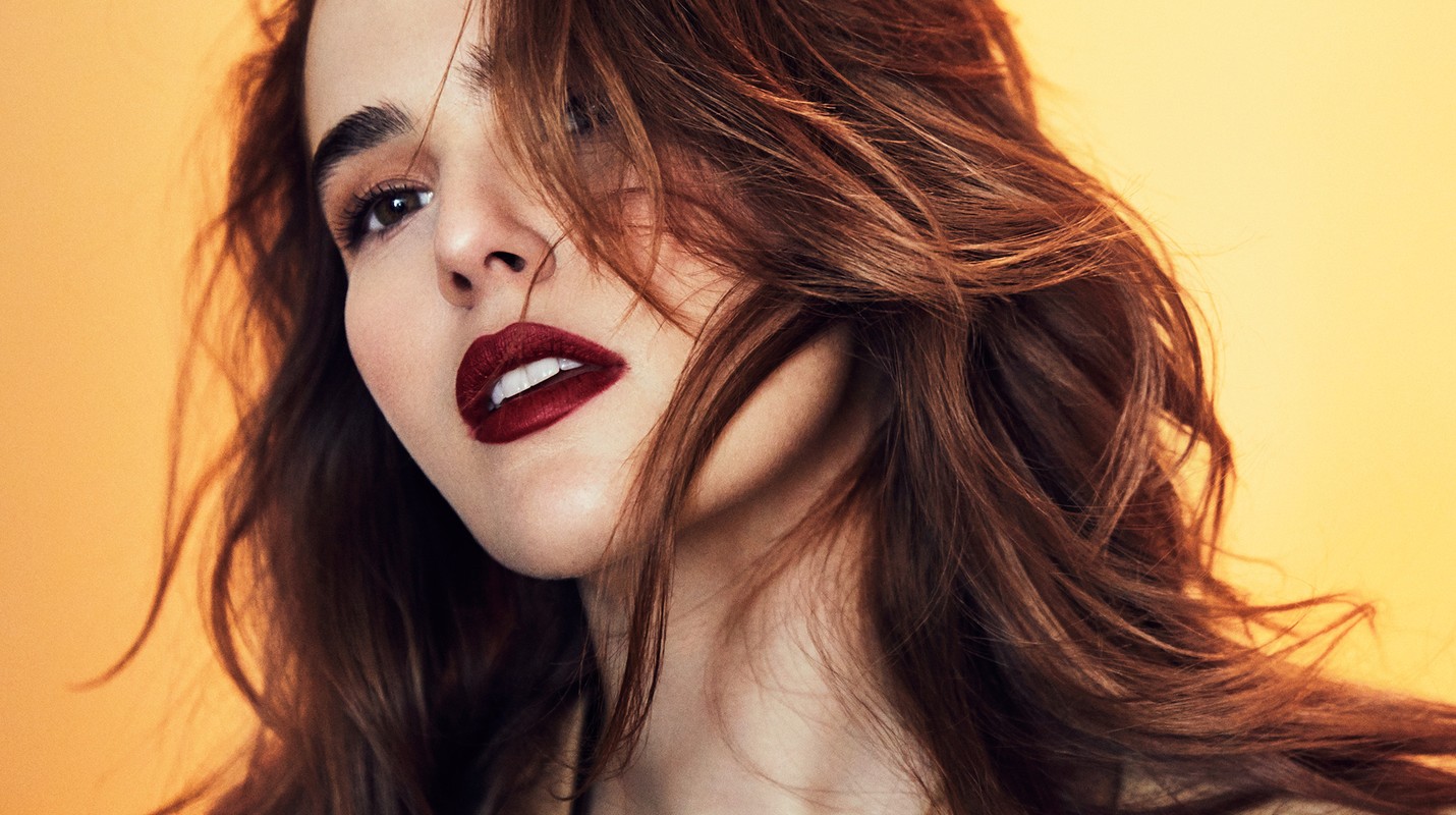 Close-up portrait of a brunette adult woman with dark red lipstick against a bright yellow background. Beauty and fashion editorial.