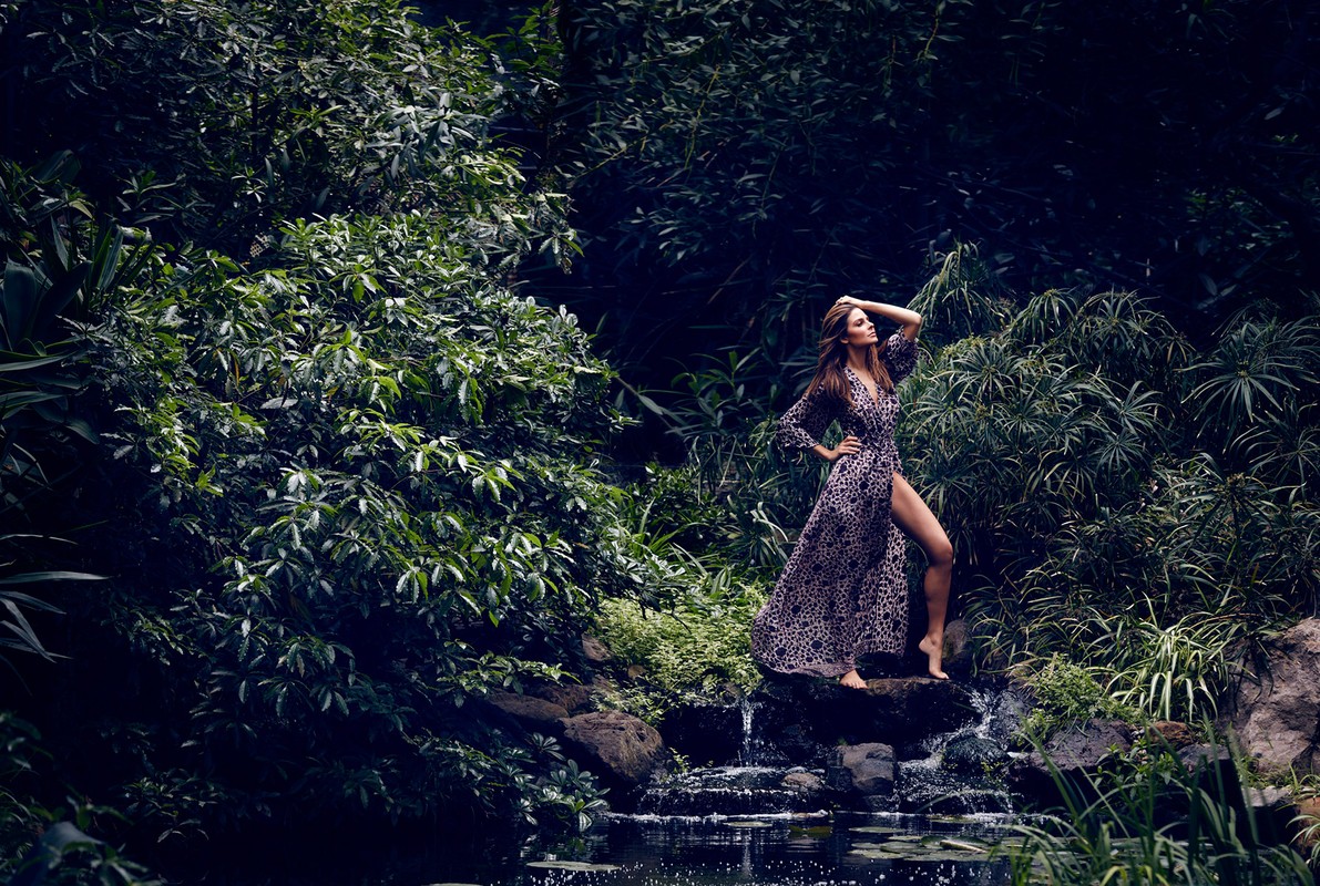 Woman in patterned dress posing on rocks by a small forest waterfall photographed by James White