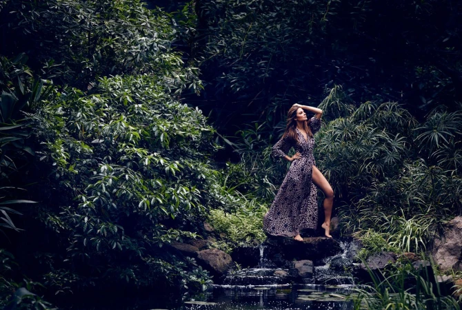 Woman in patterned dress posing on rocks by a small forest waterfall photographed by James White