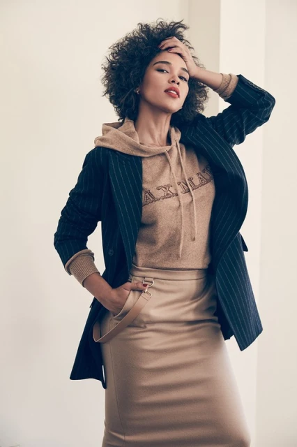 Woman in pinstripe blazer and pencil skirt posing indoors with hand in pocket, showcasing fashion and portrait photography.