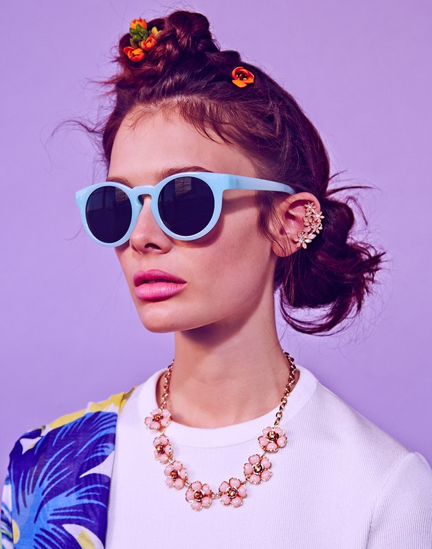 Close-up of a stylish woman wearing sunglasses and flower accessories, set against a light purple background. Fashion and beauty photography.