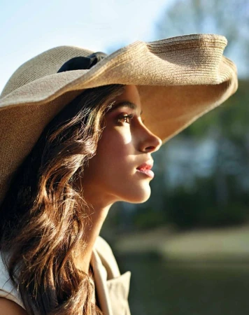 Profile portrait of a woman wearing a wide-brimmed straw hat with a black band outdoors in warm sunlight.