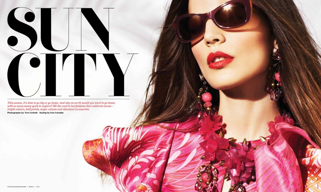 A stylish adult female wears sunglasses, bright red lipstick, and a pink floral outfit with statement earrings and a necklace in a fashion editorial.
