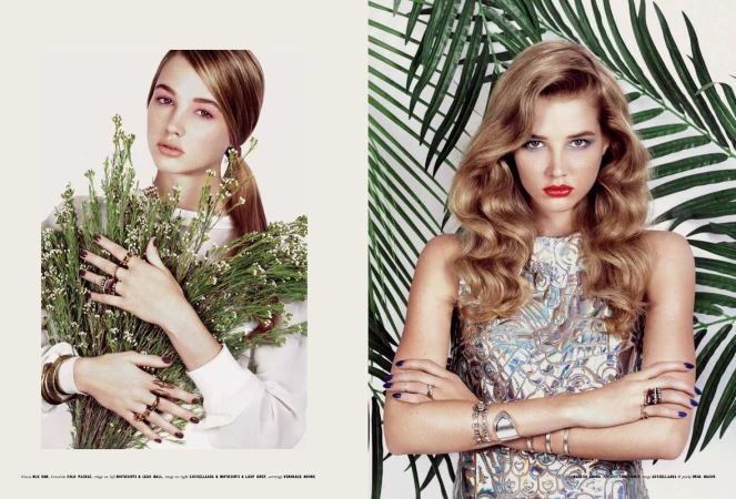 Editorial fashion shot of two young adult women wearing jewelry and makeup. One holds flowers, the other poses with tropical leaves.