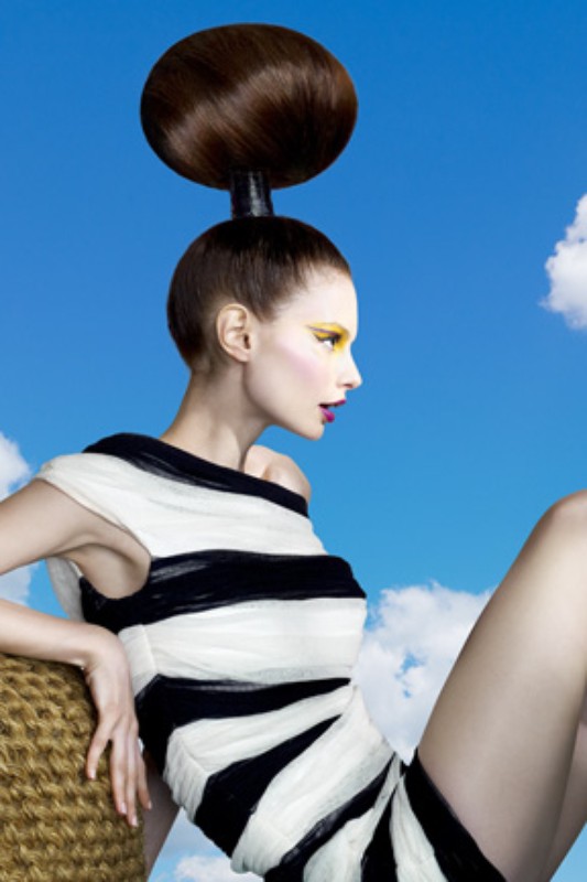 Woman with avant-garde hairstyle and striped dress poses against a sky backdrop, showcasing fashion and creative hair styling.