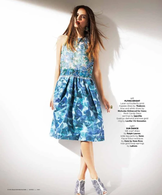 A woman poses in a blue and white printed sleeveless dress with matching heels against a white background in a studio fashion shot.