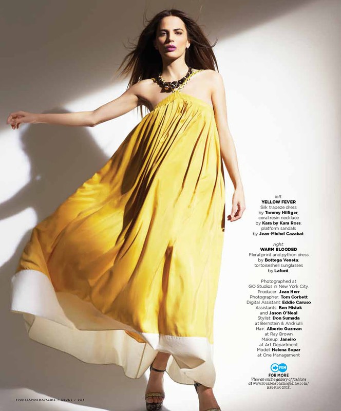 Elegant woman poses in flowing yellow dress with white trim, accessorized with necklace and sandals, against a bright, minimalist background.