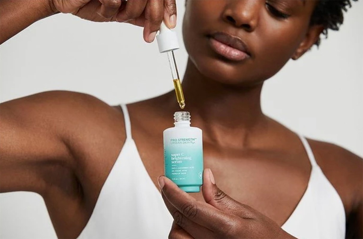 Woman holding a skincare bottle and dropper of serum. Close-up of beauty product in hand, isolated on a white background in studio lighting.
