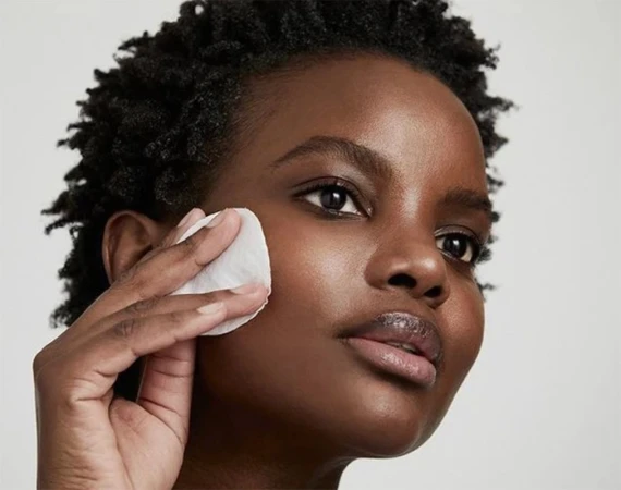 Close-up of an African American woman using a cotton pad on her face, demonstrating skincare routine in a beauty and self-care setting.