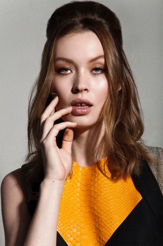 Headshot of a young adult female model with auburn hair, wearing a snakeskin-textured yellow and black dress in a photo studio setting.