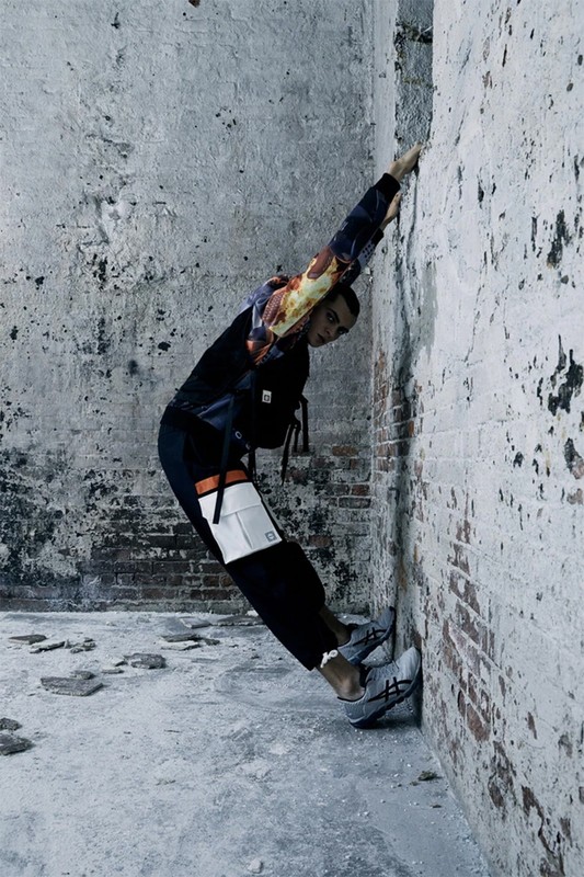 A person in athletic wear leans against a distressed concrete and brick wall, showcasing fashion in an urban environment with cool tones.