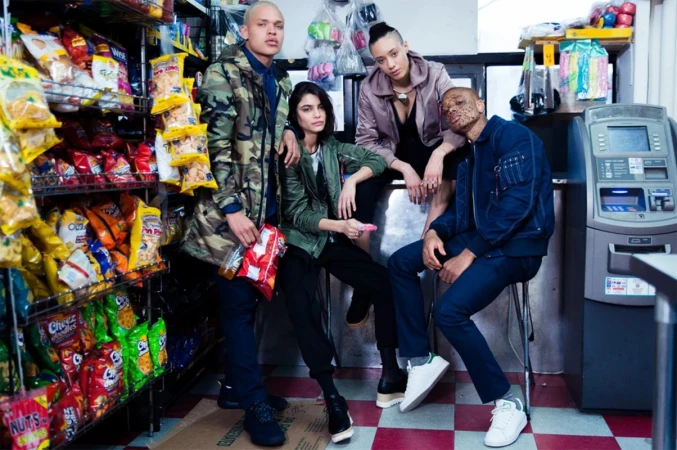Four young adults pose in a convenience store with shelves of snacks, wearing bomber jackets and trendy outfits, captured in a medium shot.