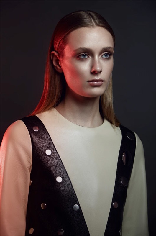 Portrait of an adult female with long blonde hair and a neutral facial expression wearing a sleeveless leather studded vest.