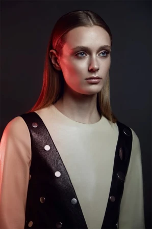Portrait of an adult female with long blonde hair and a neutral facial expression wearing a sleeveless leather studded vest.