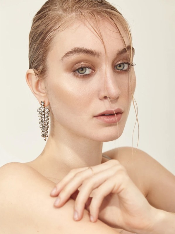Close-up portrait of a woman wearing ornate crystal drop earrings with damp hair framing her face against a neutral background