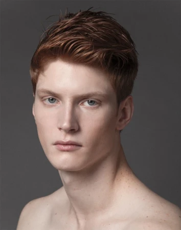 Close-up portrait of a young man with short textured reddish-brown hair against a solid grey background