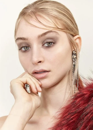 Close-up portrait of a woman with light hair and light skin wearing long, dangling earrings and a red, faux fur stole, indoors.