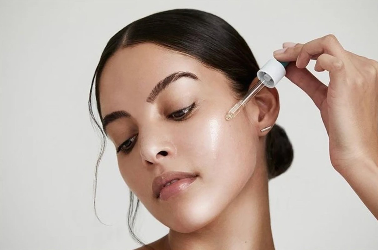 Close-up of a woman applying face serum with a dropper, highlighting skincare and beauty, with a soft, clean aesthetic.