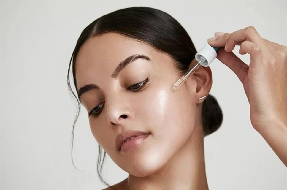 Close-up of a woman applying face serum with a dropper, highlighting skincare and beauty, with a soft, clean aesthetic.