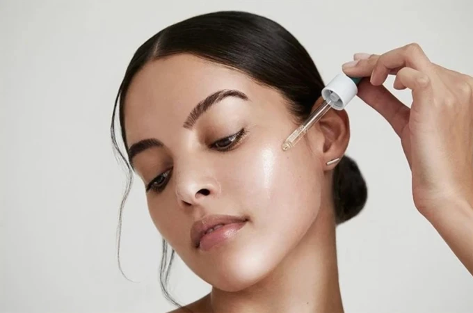 Close-up of a woman applying face serum with a dropper, highlighting skincare and beauty, with a soft, clean aesthetic.
