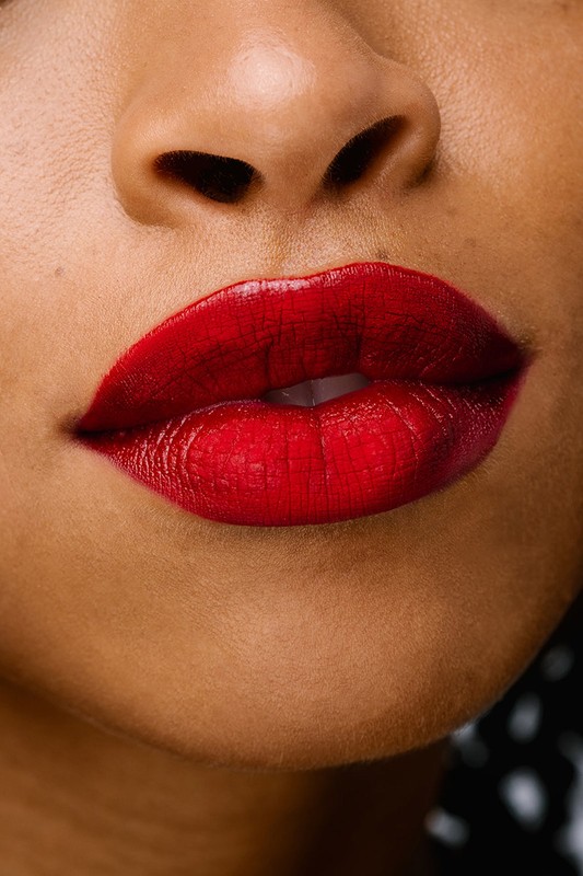 Close-up of an adult female with medium skin tone wearing vibrant red lipstick, highlighting beauty and fashion. Cropped face view.