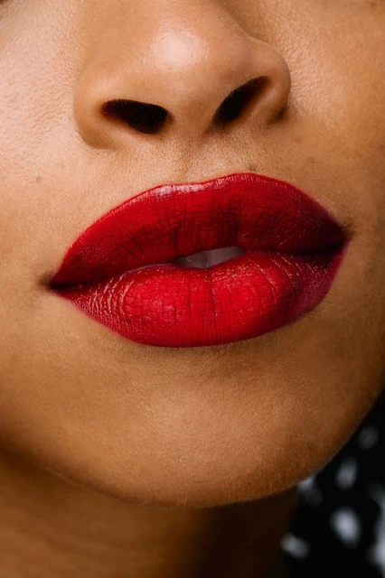 Close-up of an adult female with medium skin tone wearing vibrant red lipstick, highlighting beauty and fashion. Cropped face view.