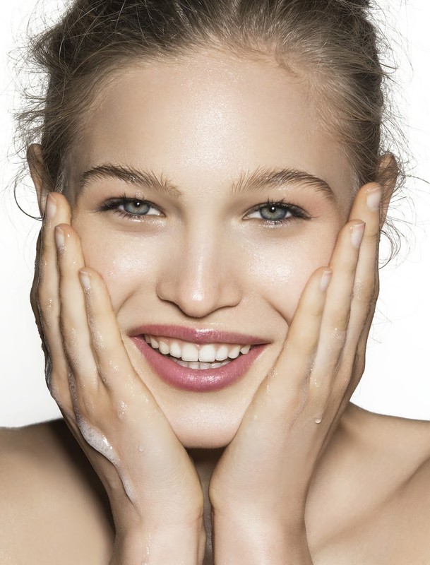 Close-up studio shot of a smiling woman with her hands framing her face, showcasing skincare and natural beauty against a white backdrop.