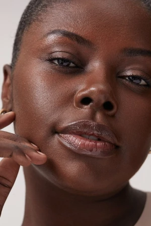 Close-up portrait of a Black woman with natural skin texture and glossy lips, styled by make-up artist Jen Fiamengo