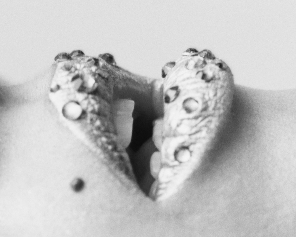 Close-up black and white shot of a person's navel piercing with circular jewelry, showing the texture of the skin and surrounding area.