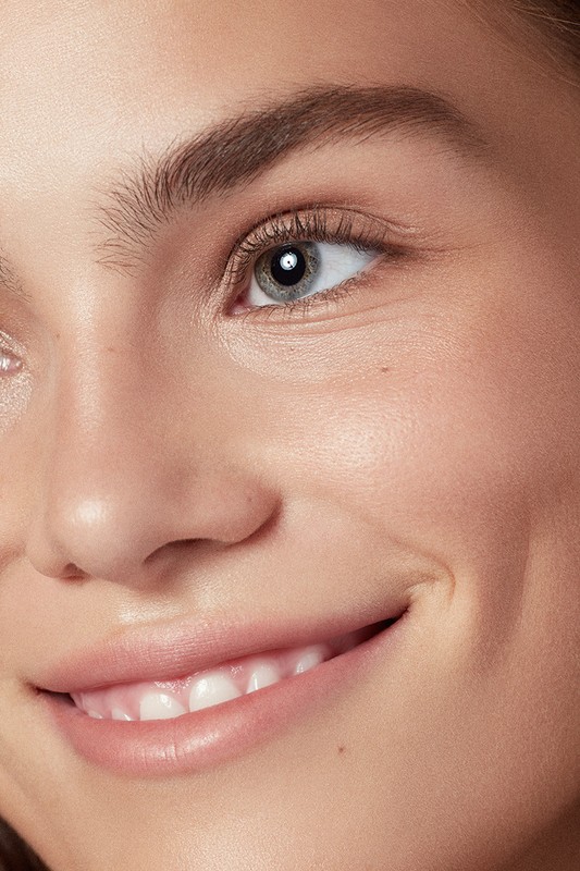 Close-up portrait of a young woman with light skin, blue eyes, and a warm smile, focusing on her facial features and expression.