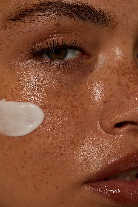 Close-up portrait of a freckled face with a dab of white cream on the cheek and natural makeup by Jen Fiamengo