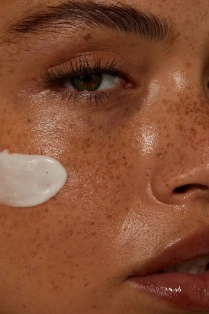 Close-up portrait of a freckled face with a dab of white cream on the cheek and natural makeup by Jen Fiamengo