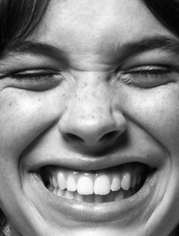 Close-up black and white portrait of a smiling woman with eyes closed, showcasing her teeth and facial expression.