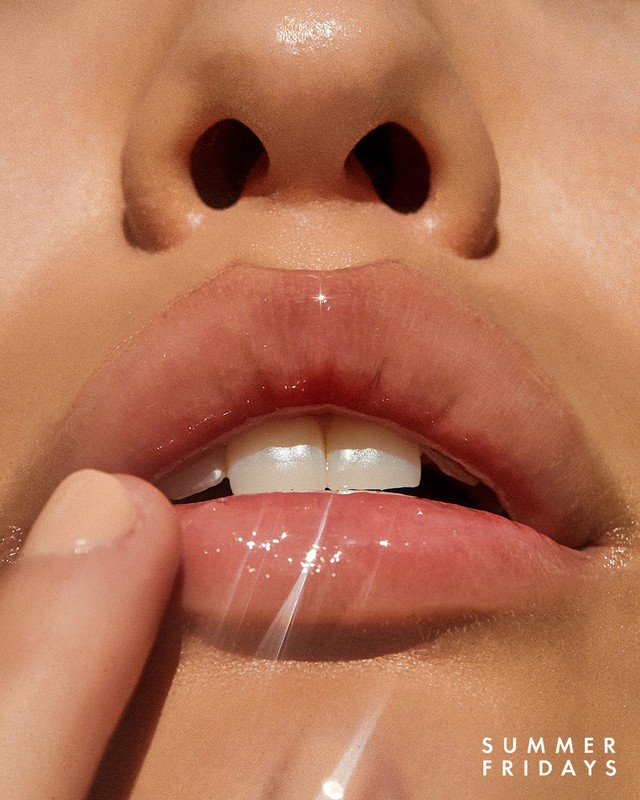 Close-up of a woman's face features; full lips, teeth, and finger touching lip. Soft lighting, glossy lips, beauty shot, minimal background.